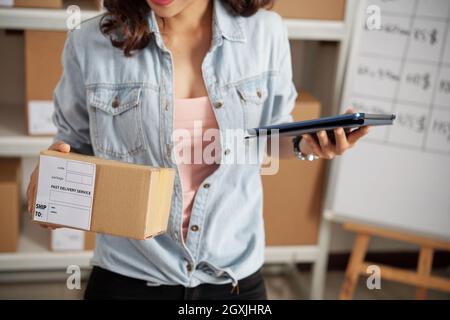 Close-up of unrecognizable woman in denim shirt using tablet while searching number of parcel in office Stock Photo