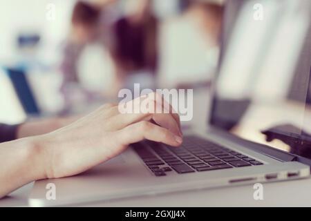 close up of business womans hand typing on laptop  at modern startup office computer, blured team in meeting, people group in background Stock Photo