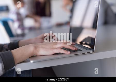 close up of business womans hand typing on laptop  at modern startup office computer, blured team in meeting, people group in background Stock Photo