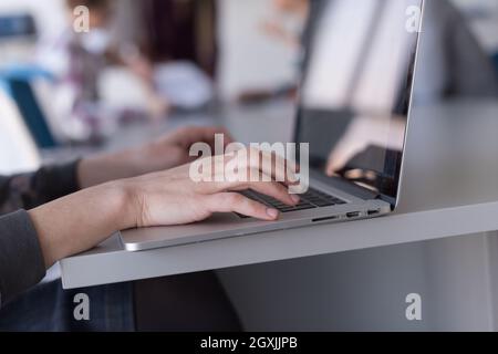 close up of business womans hand typing on laptop  at modern startup office computer, blured team in meeting, people group in background Stock Photo