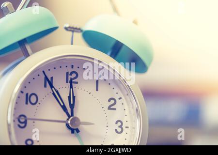 Alarm clock is standing on a grey desk, books in the blurry background Stock Photo