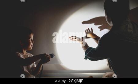 Toned photo of young mother and little boy playing in theater of shadows before going to sleep at night. Stock Photo