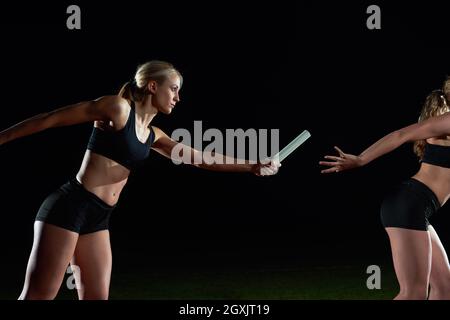 woman athletic runners passing baton in relay race Stock Photo