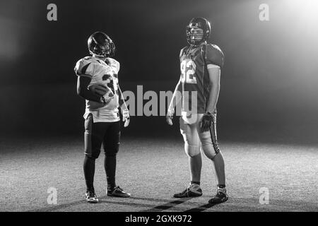 portrait of confident American football players holding ball while standing on field at night Stock Photo