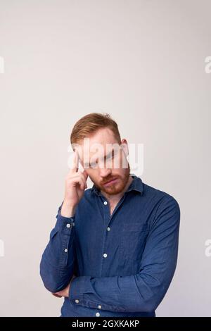 Serious young redhead man with beard focused on thoughts touching forehead against gray background Stock Photo