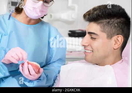 Orthodontist holding invisible retainer for teeth alignment. In clinic shows patient removable transparent plastic aligners or invisalign use and benefit. High quality photo. Stock Photo