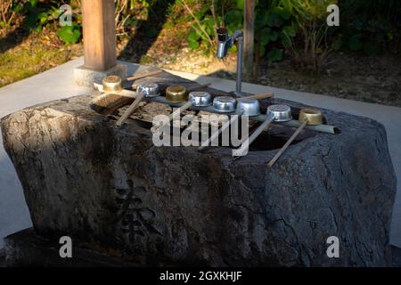 Ladles or hishaku arranged over a stone basin or temizuya at the entrance of Kanjizai-ji Buddhist temple, Ainan, Ehime Prefecture, Japan Stock Photo