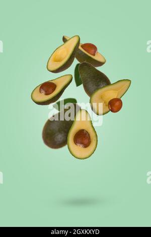 Creative food concept with  fresh ripe whole and sliced avocado flying in air isolated on green background. Healthy food, diet, tropical exotic fruit, Stock Photo