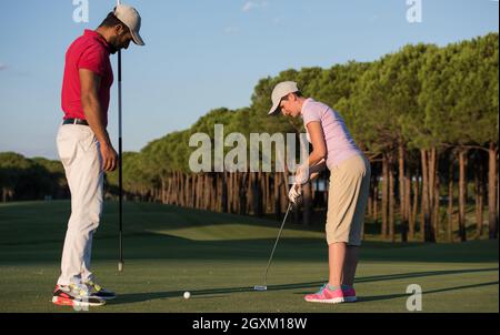 male golf instructor teaching female golf player, personal trainer giving lesson on golf course Stock Photo