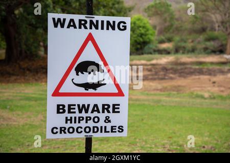 Close up on a sign reading 'Warning beware of hippo and crocodiles. There is also a visual reference to a hippo and a crocodile in a red triangle. Stock Photo