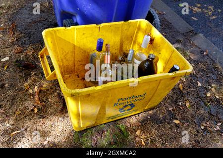 A yellow recycling tub labelled "Portland Recycles!" filled with glass bottles and jars. In Portland, glass is recycled separately from the mixed ... Stock Photo