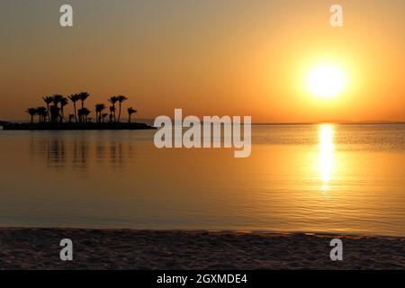 Beautiful place for privacy. Sunset over island in sea. Bright sun during dawn over the sea. Island with palm trees and benches in ocean. Summer vacat Stock Photo