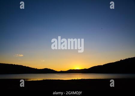 Sunset on lake in mountains with golden glow and dark blue sky Stock Photo