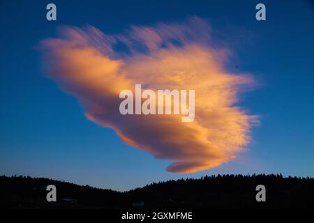 Large pink and white cloud in blue sky with mountain silhouette Stock Photo