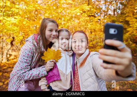 a cheerful woman takes selfies with her daughters in an autumn park