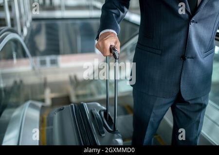 Man holding suitcase on escalator going up Stock Photo