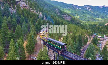 Locomotive train with passengers going through pine trees in mountain Stock Photo