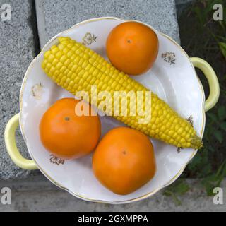 Close-up top view of boiled with corncob sweet corn and just washed orange tomatoes on white plate. Stock Photo
