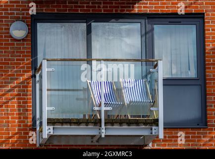 two blue and white striped deckchairs on the balcony of a small modern flat in southampton. garden chairs set out in a small outdoor space. Stock Photo