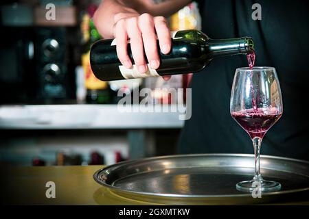 Waiter putting wine, in a glass on a typical metal tray, inside the bar Stock Photo