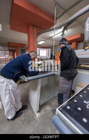 two young carpenters calculating and programming a cnc wood working machine in workshop. wood workers preparing a computer program for CNC machine at Stock Photo