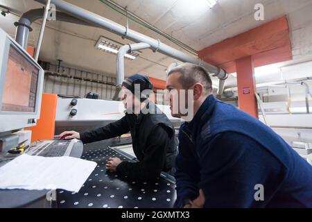 two young carpenters calculating and programming a cnc wood working machine in workshop. wood workers preparing a computer program for CNC machine at Stock Photo