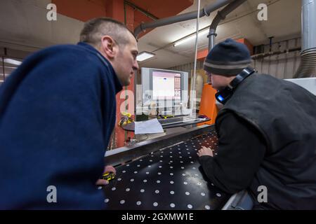 two young carpenters calculating and programming a cnc wood working machine in workshop. wood workers preparing a computer program for CNC machine at Stock Photo
