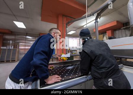 two young carpenters calculating and programming a cnc wood working machine in workshop. wood workers preparing a computer program for CNC machine at Stock Photo