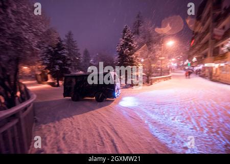 Electric taxi bus on snowy streets in the car-free Alpine mountain village at cold winter night Stock Photo