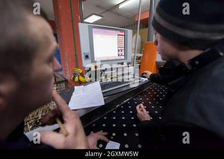 two young carpenters calculating and programming a cnc wood working machine in workshop. wood workers preparing a computer program for CNC machine at Stock Photo