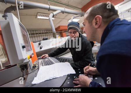 two young carpenters calculating and programming a cnc wood working machine in workshop. wood workers preparing a computer program for CNC machine at Stock Photo