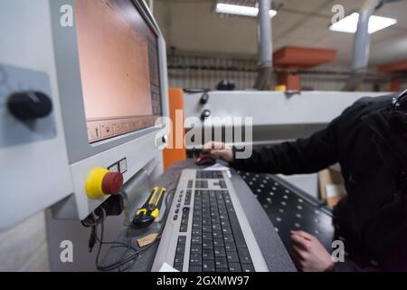 two young carpenters calculating and programming a cnc wood working machine in workshop. wood workers preparing a computer program for CNC machine at Stock Photo