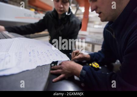 two young carpenters calculating and programming a cnc wood working machine in workshop. wood workers preparing a computer program for CNC machine at Stock Photo