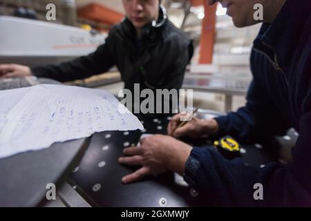 two young carpenters calculating and programming a cnc wood working machine in workshop. wood workers preparing a computer program for CNC machine at Stock Photo