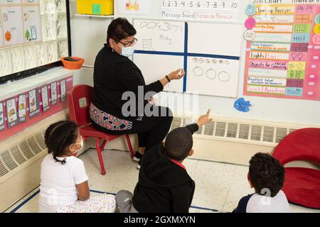 Education Preschool 4-5 year olds morning meeting, boy pointing to answer question, teacher and children wearing face masks to protect vs Covid-19 Stock Photo