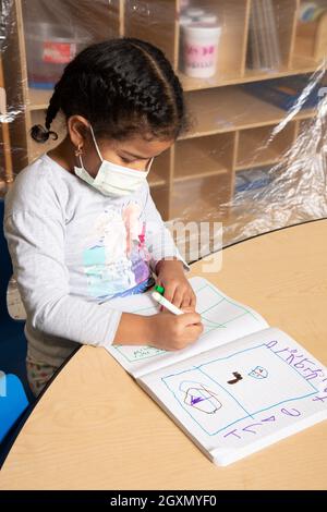 Education Preschool 4-5 year olds girl drawing in notebook using marker, tripod grip, wearing mask to protect vs Covid-19 virus Stock Photo