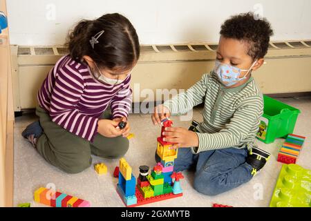 Education Preschool 3-4 year olds boy and girl playing together with connecting plastic blocks (Duplo), wearing face masks to protect against Covid-19 Stock Photo