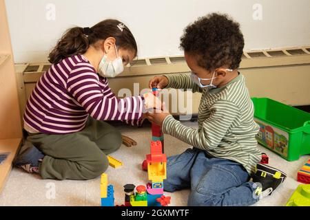 Education Preschool 3-4 year olds boy and girl playing together with connecting plastic blocks (Duplo), wearing face masks to protect against Covid-19 Stock Photo
