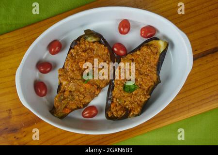 Stuffed Eggplants, Aubergines with Bolognese sauce and Fresh cherry tomatoes in a ceramc platter on a green tablecloth. Top view Stock Photo