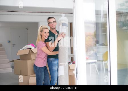 Young couple carrying a carpet moving in to new home together. Home, people, moving and real estate concept Stock Photo