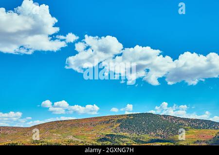 Blue sky with small clouds against colorful hill Stock Photo
