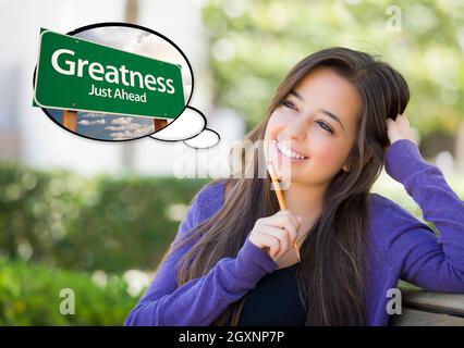 Pensive Young Woman with Thought Bubble of Greatness Just Ahead Green Road Sign. Stock Photo