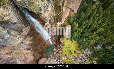 Looking down at large waterfall from cliffs into mossy rocks and pine trees Stock Photo