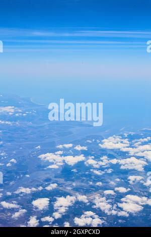 Airplane view of clouds and blue sky with land in distance Stock Photo
