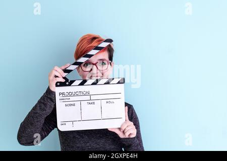 redhead woman holding movie clapper against cyan background cinema concept Stock Photo