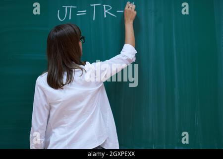 an attractive teacher with glasses explains to the students how to do the task on the board Stock Photo
