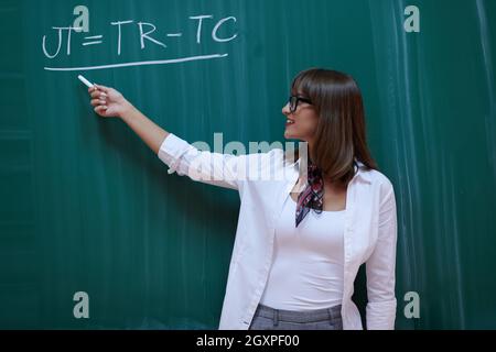 an attractive teacher with glasses explains to the students how to do the task on the board Stock Photo