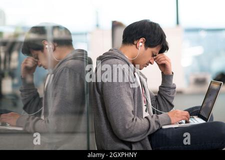 young indian software developer man using laptop computer writing programming code while sitting on the floor at modern creative startup office Stock Photo