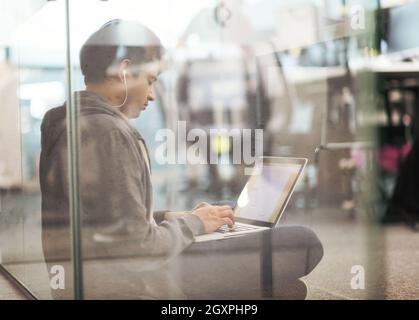 young indian software developer man using laptop computer writing programming code while sitting on the floor at modern creative startup office Stock Photo