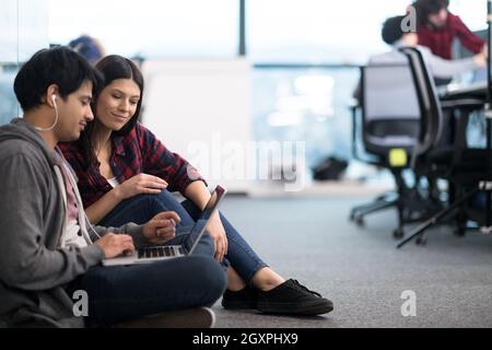young software developers couple using laptop computer writing programming code while sitting on the floor at modern creative startup office Stock Photo